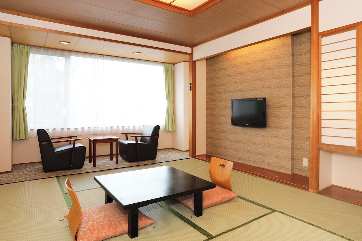 A traditional Japanese room with tatami flooring, a low table, chairs, a television, and a sliding door.