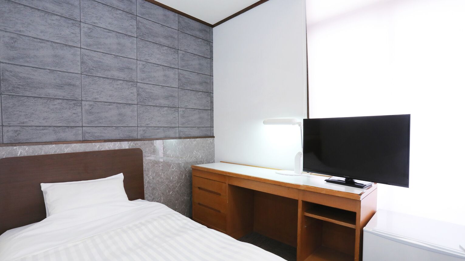 Een hotelkamer met een bed, een houten bureau, een televisie en een grote spiegel.