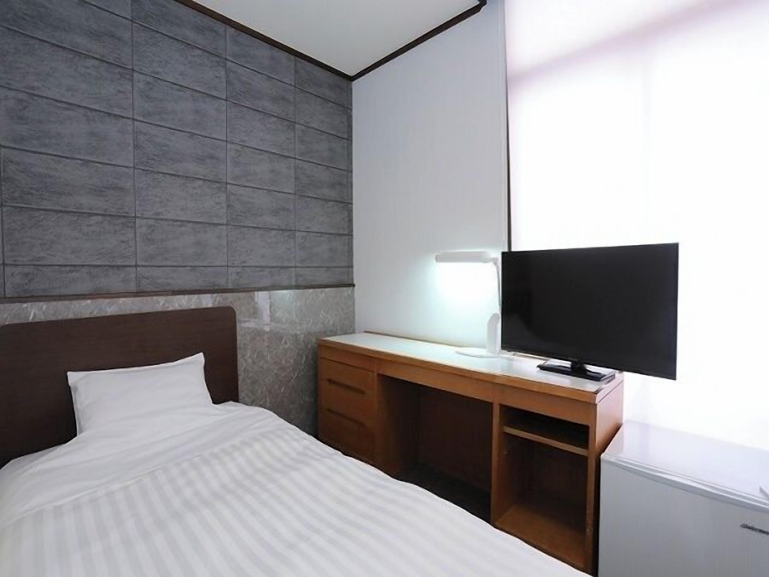 Habitación de hotel con una cama, un escritorio con ordenador y televisión.