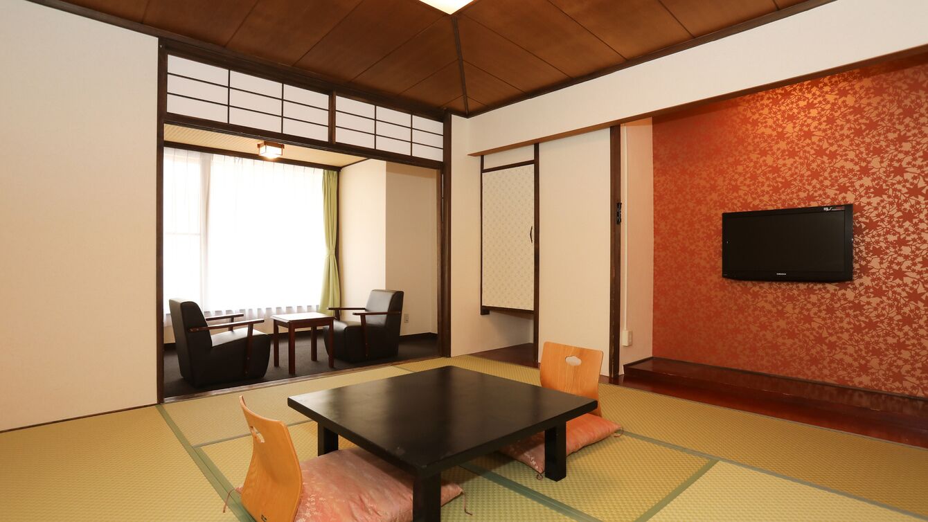 Een traditionele Japanse kamer met tatami vloerbedekking, een lage tafel, stoelen, een televisie en schuifdeuren.