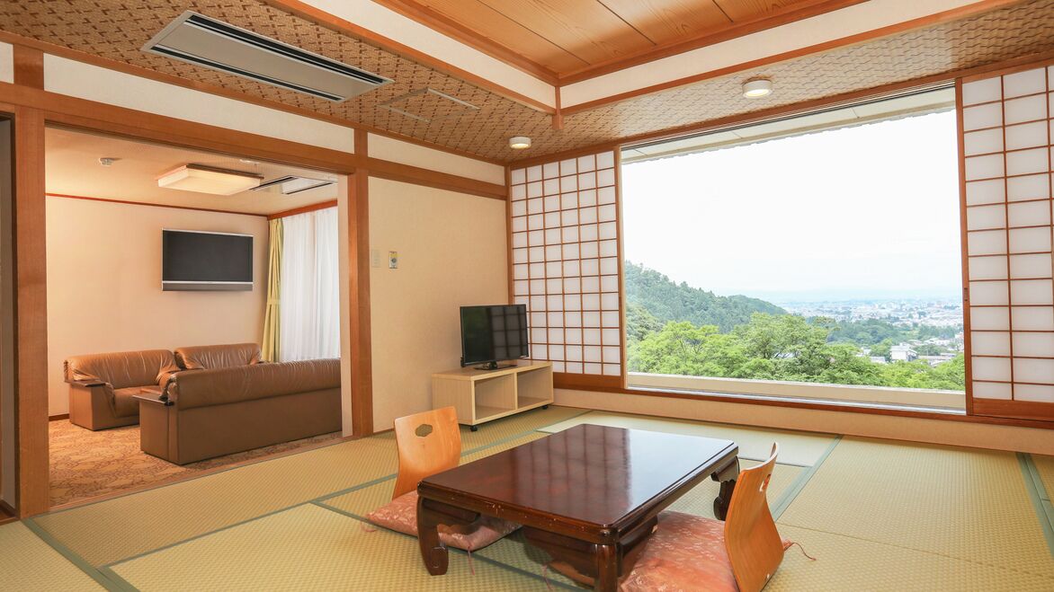 Een traditionele Japanse kamer met tatami vloeren, een lage tafel, een bank, een televisie en een groot raam met uitzicht op groen.