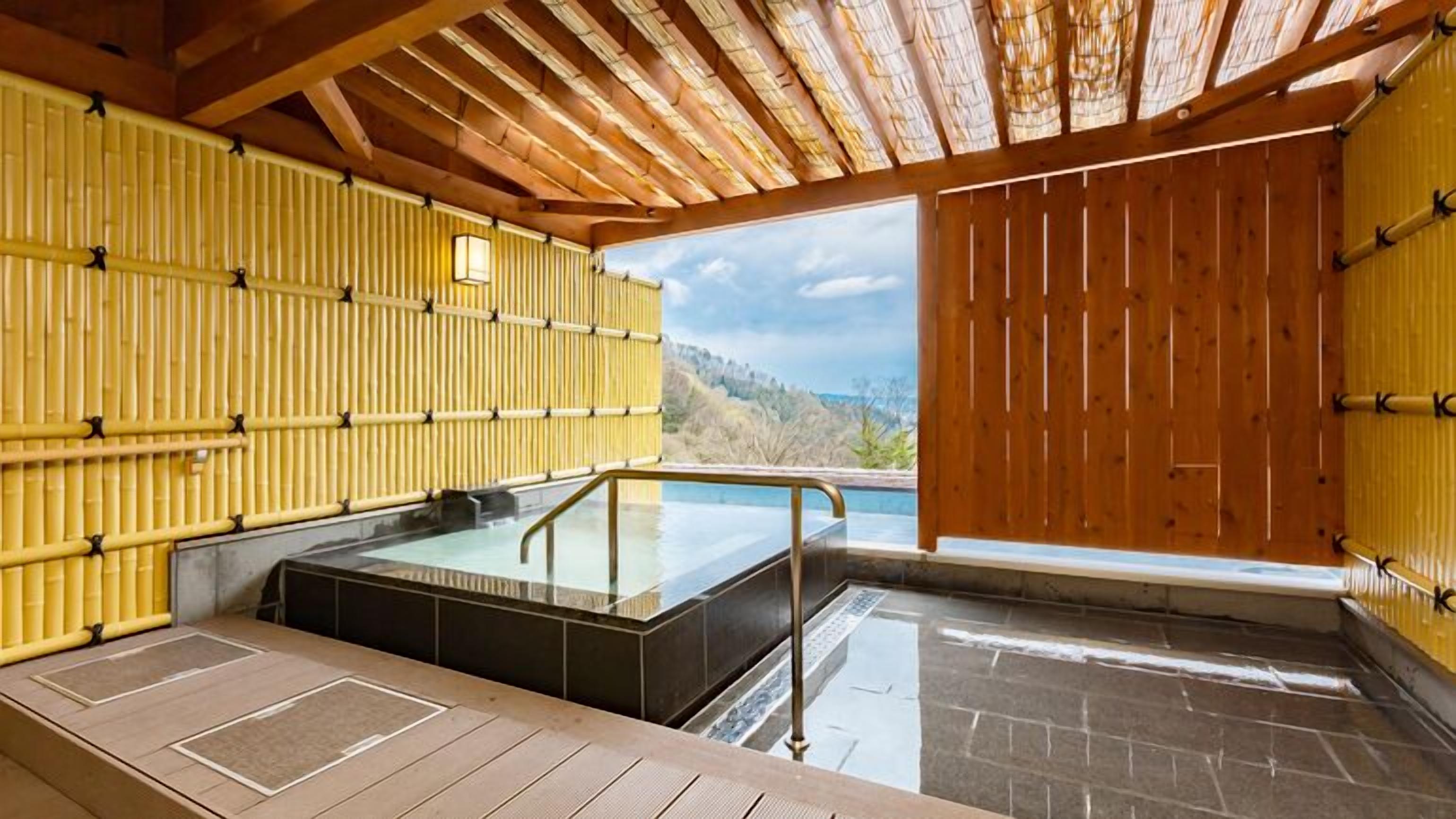 Een traditioneel Japans onsen met een houten inrichting, een door glas omheemd warmwaterbron en uitzicht op de bergen.