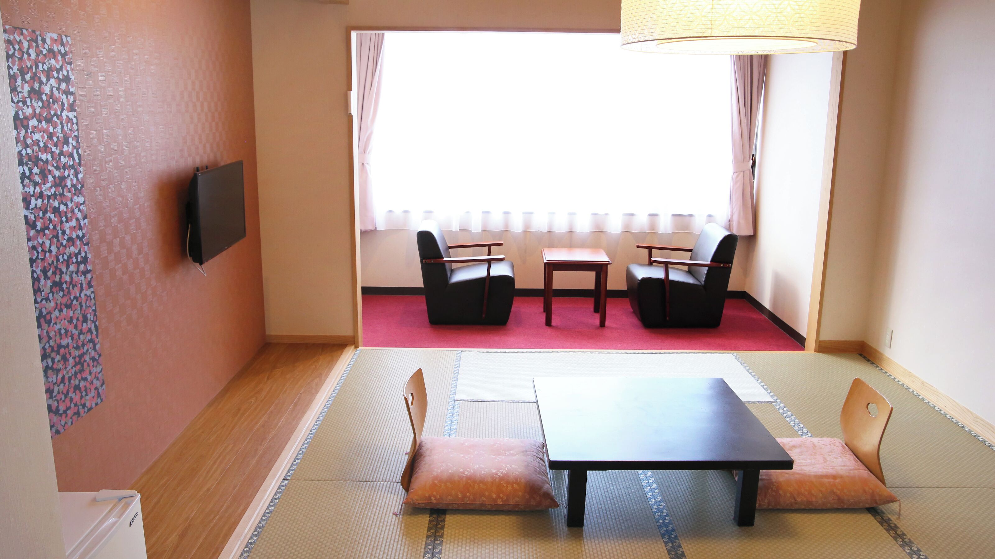Una habitación con esteras de tatami, una mesa baja, dos sillas, un televisor y una ventana con cortinas.