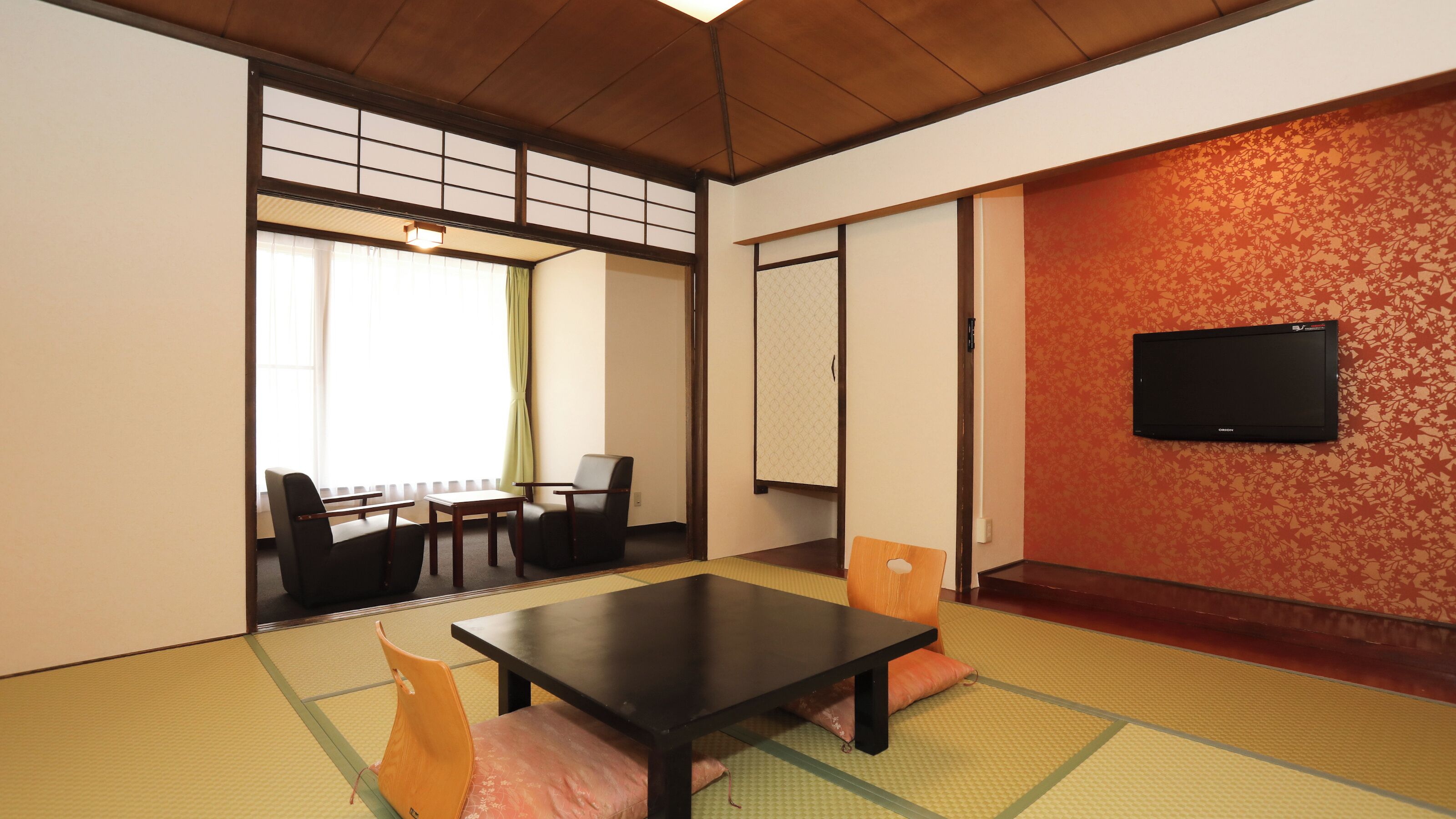 Una habitación japonesa tradicional con suelo de tatami, una mesa baja, sillas, un televisor y puertas correderas.