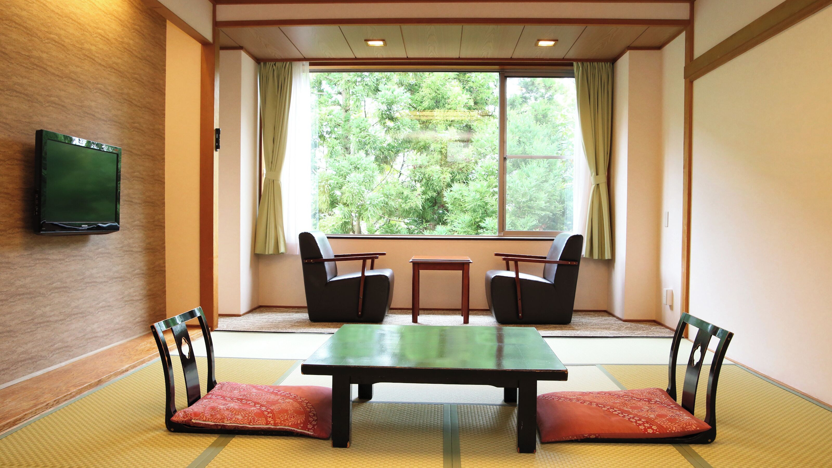 Una habitación con esteras de tatami, una mesa baja, dos sillas y un televisor en la pared.