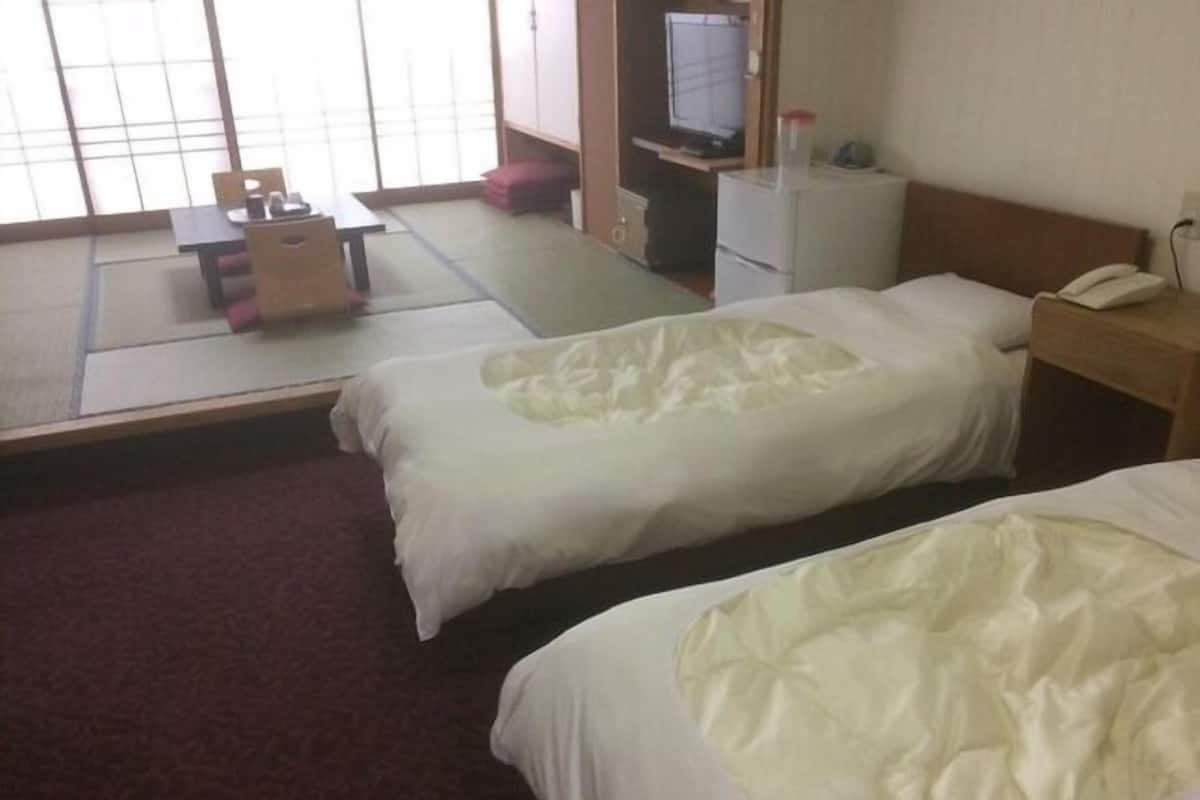 Habitación de hotel con dos camas, televisor, escritorio con teléfono y una pequeña mesa con sillas.