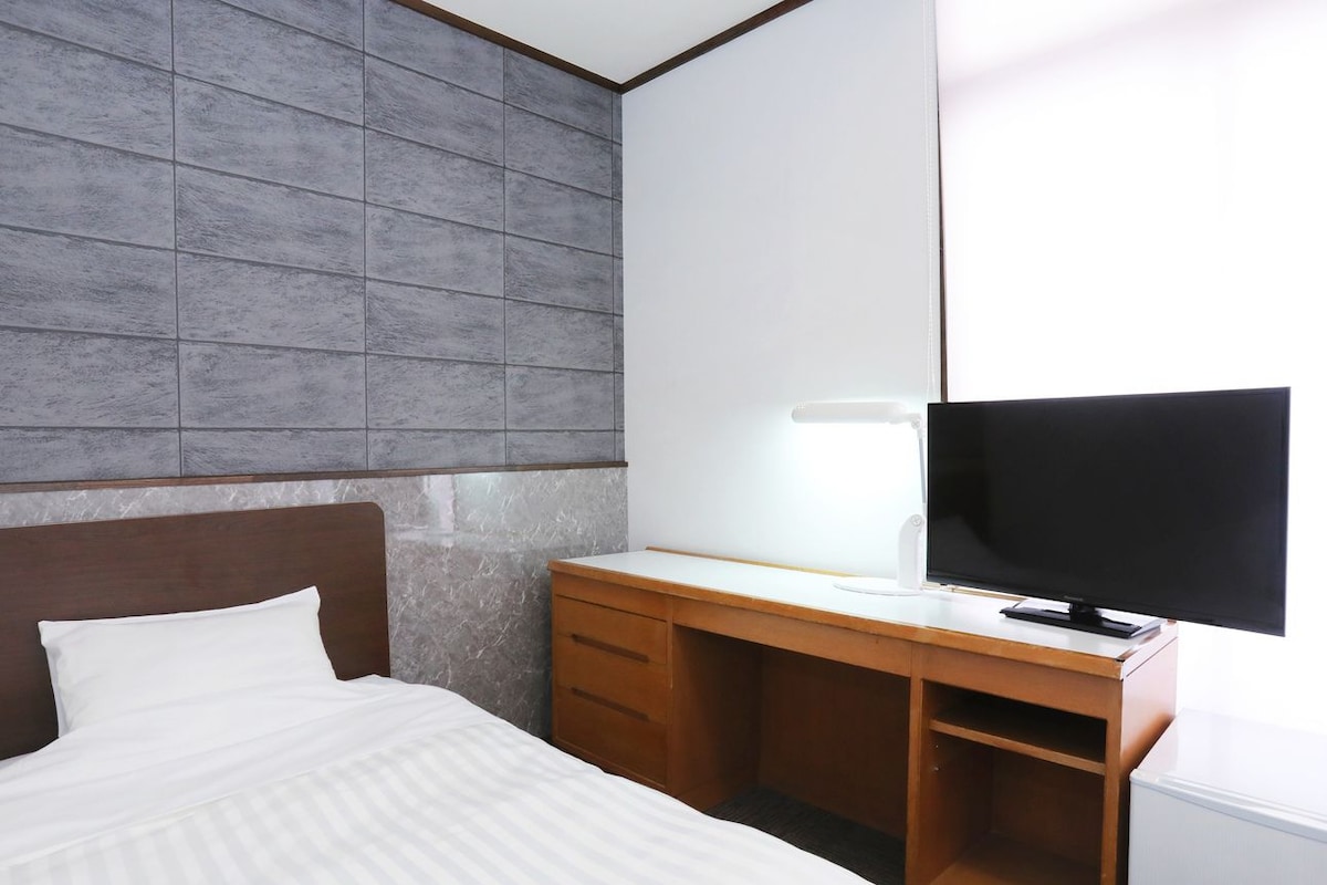 A hotel room with a bed, a wooden desk, a television, and a large mirror.