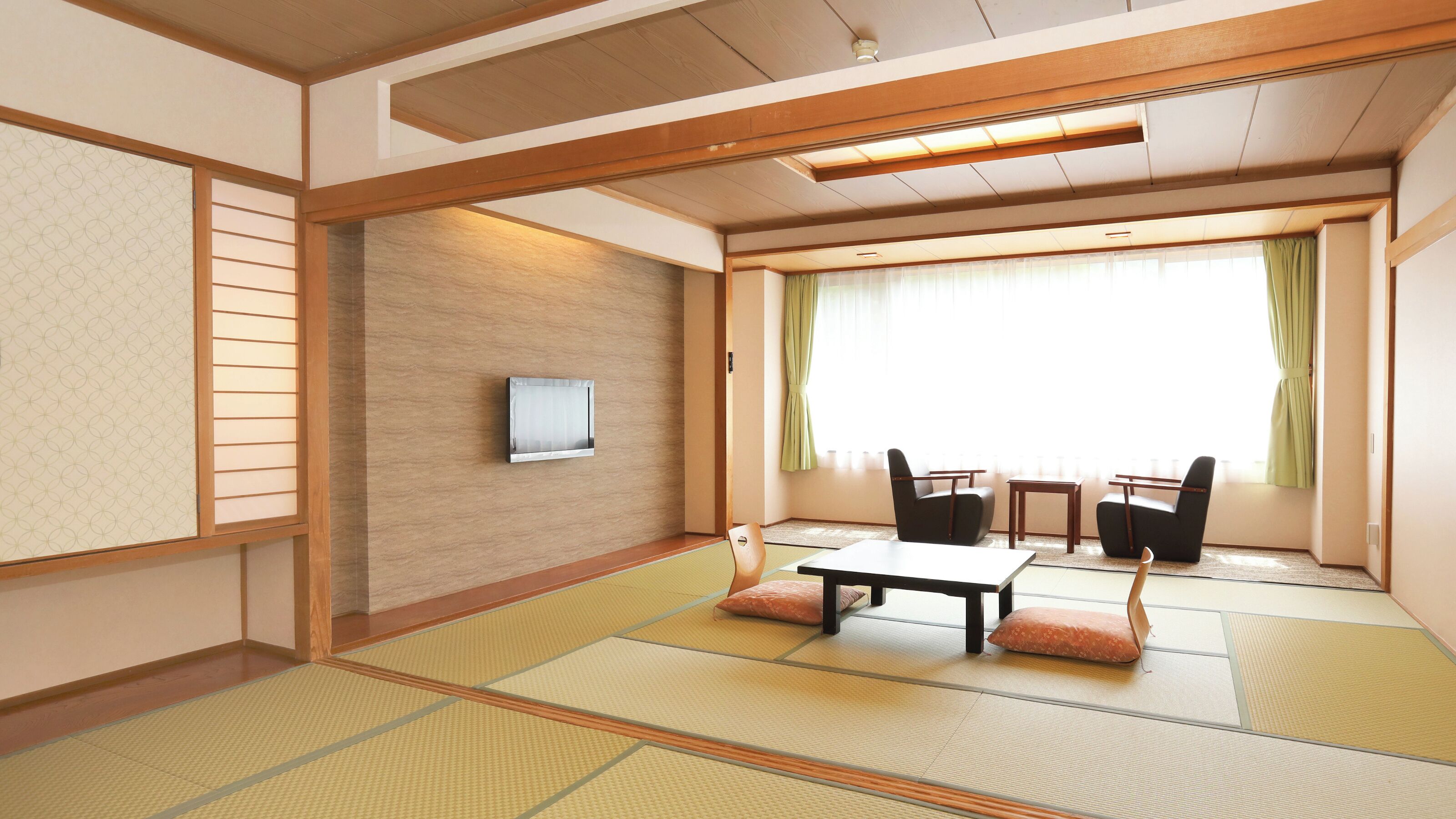 Una habitación japonesa tradicional con suelo de tatami, una mesa baja, sillas, un televisor y una ventana con cortinas.