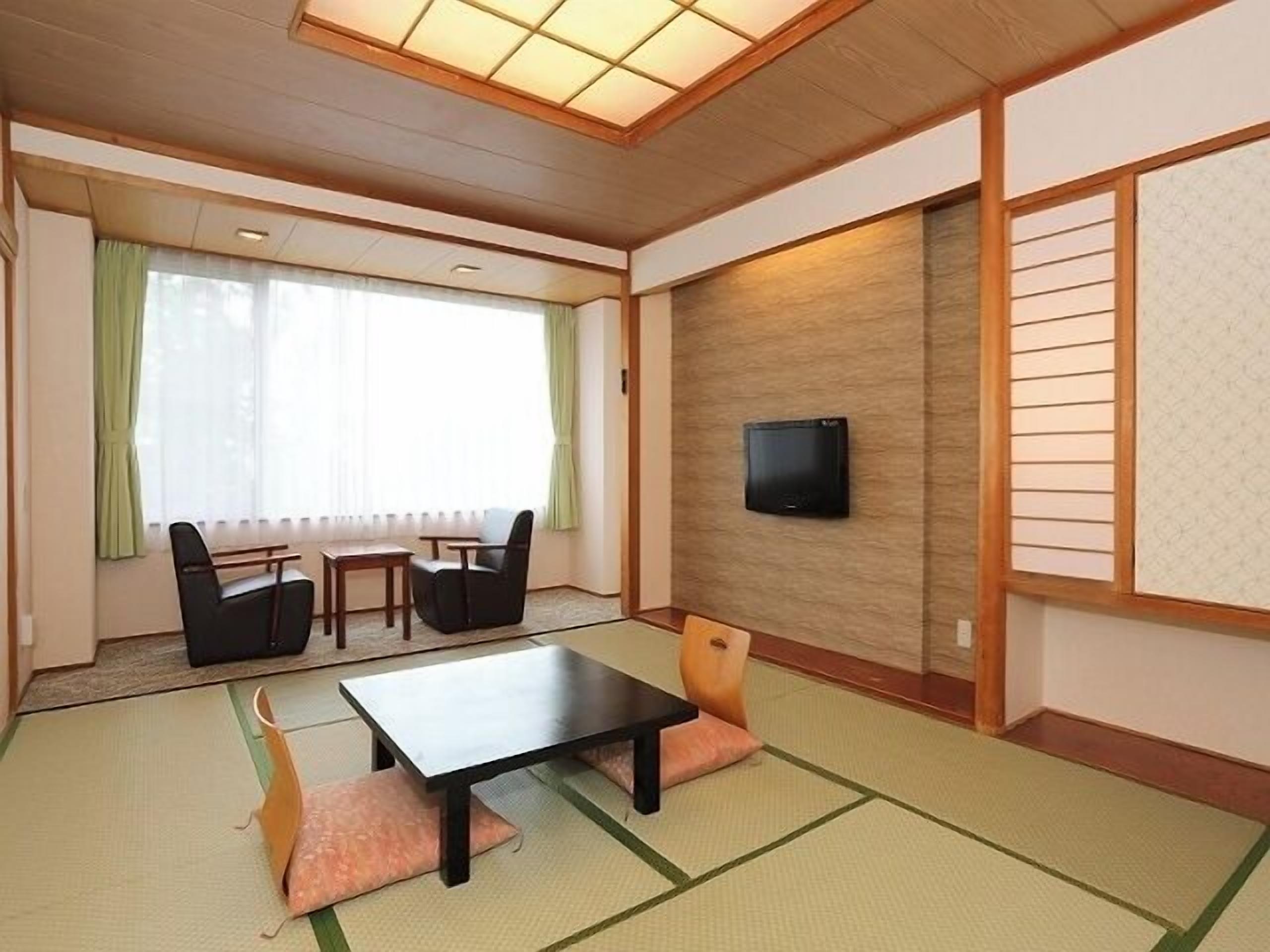 Una habitación tradicional japonesa con suelo de tatami, una mesa baja, sillas, un televisor y una puerta corredera.
