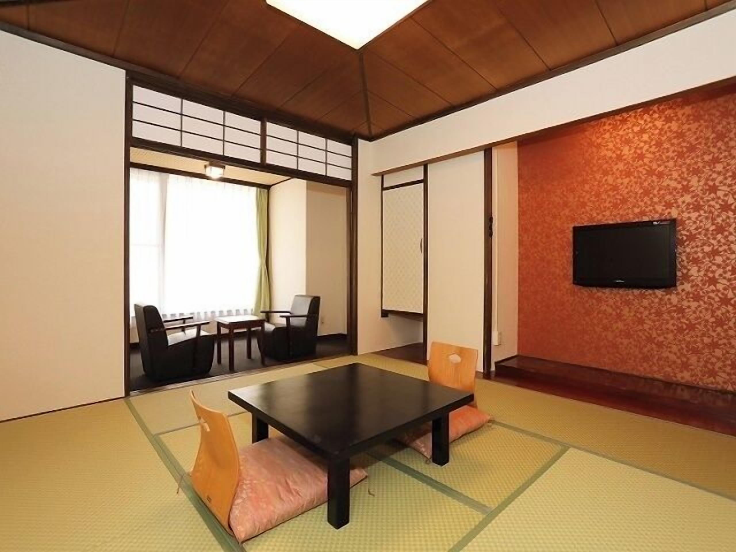 Una habitación tradicional japonesa con suelo de tatami, una mesa baja y un televisor montado en la pared.