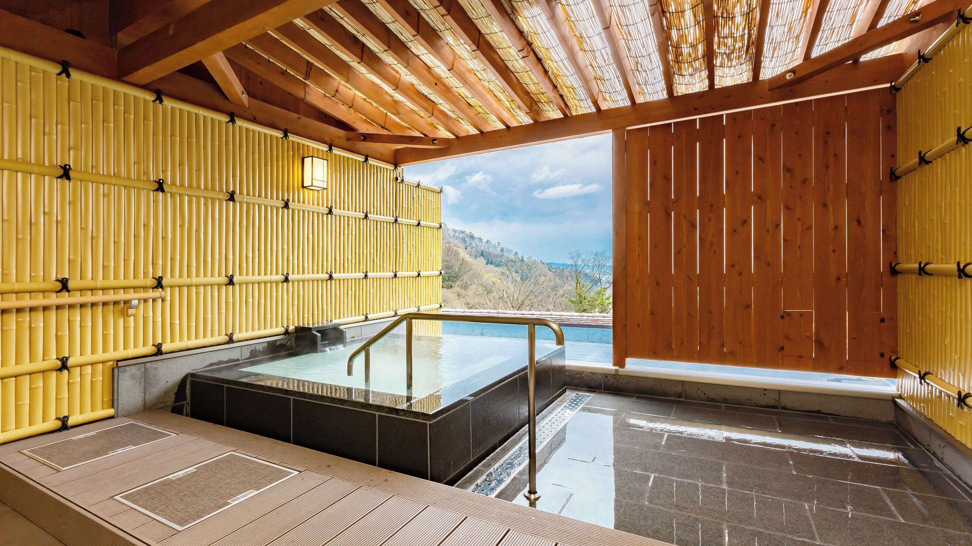 Un onsen japonés tradicional con interior de madera, una fuente termal de piedra y vistas a un paisaje montañoso.