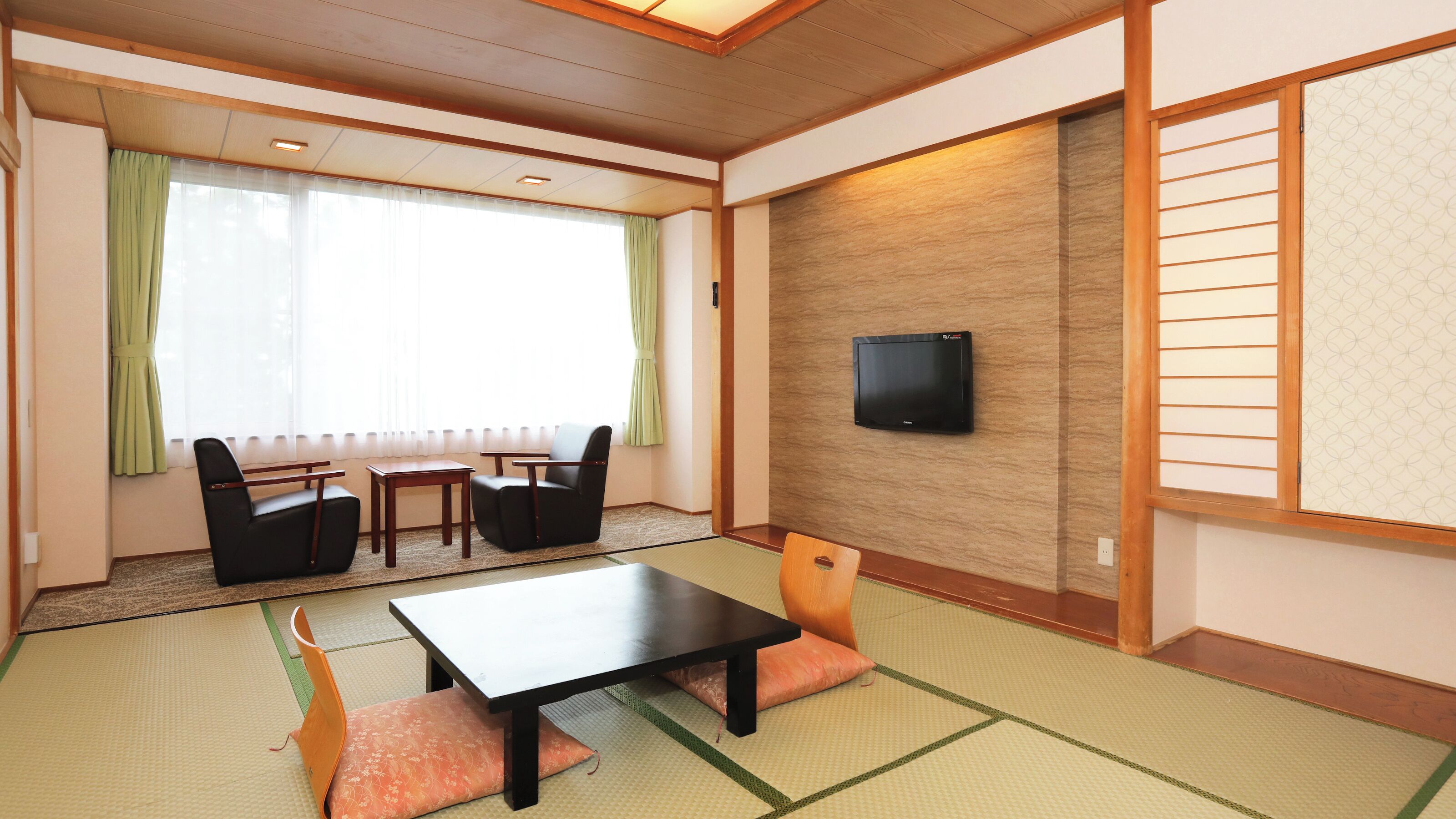 Una habitación tradicional japonesa con suelo de tatami, una mesa baja, sillas, un televisor y una puerta corredera.