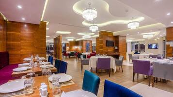 A modern dining area with multiple tables and chairs, featuring a wooden panel wall and a ceiling with circular light fixtures.