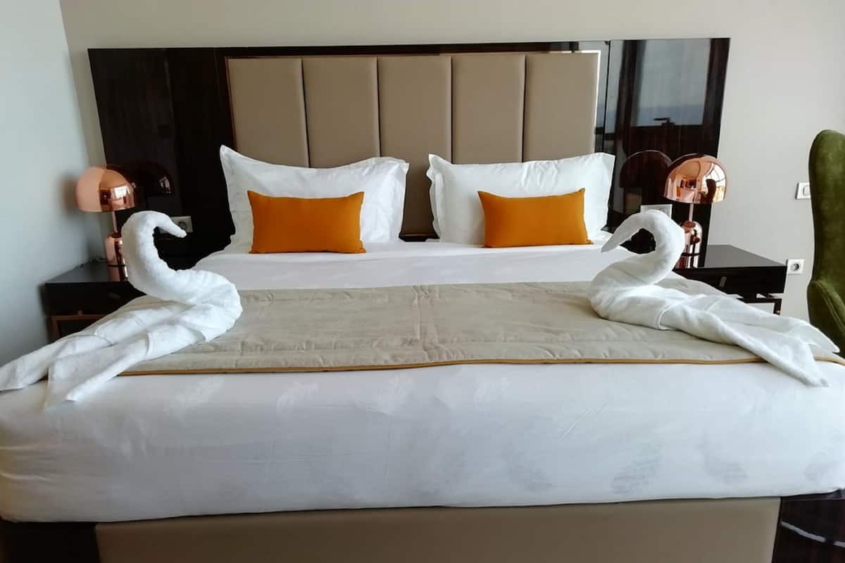 A hotel room with a large bed, two white swan-shaped towels, and a headboard with a mirror.