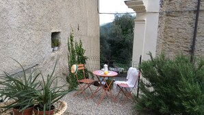 A small outdoor seating area with a table and chairs, surrounded by potted plants and a stone wall.