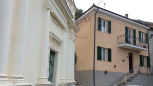 A building with a white facade and green shutters, featuring a staircase leading to a balcony.