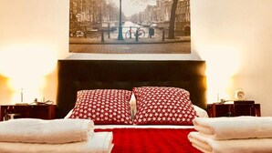 Habitació d'hotel amb un llit gran, almoinades vermelles amb dibuixos i una vista de la ciutat a la paret.
