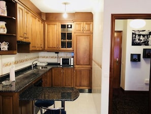 Compact kitchen with microwave, sink, and small island with chair.