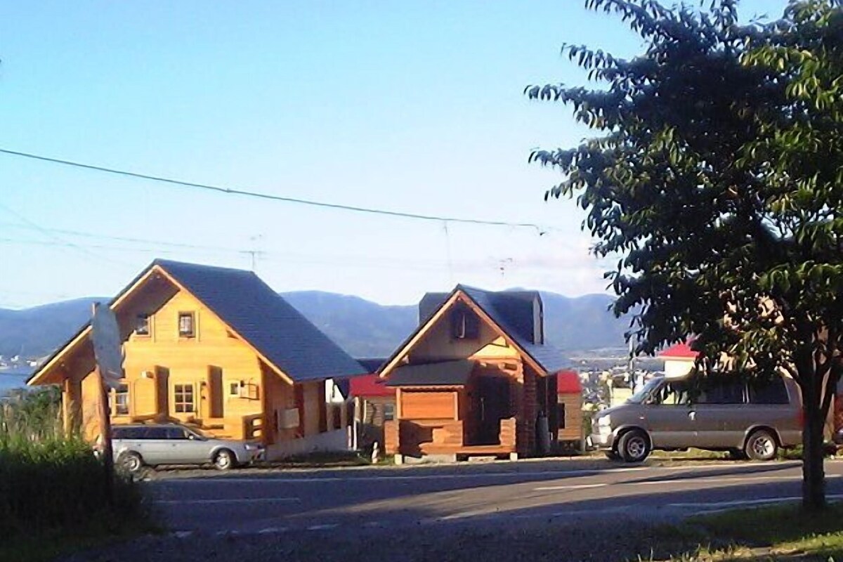 A two-story wooden house with a garage, a car parked in front, and a van parked on the street.
