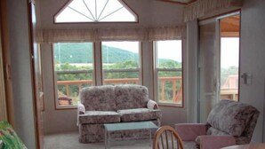 A room with a sofa, a chair, a table, and large windows offering a view of a balcony and greenery.