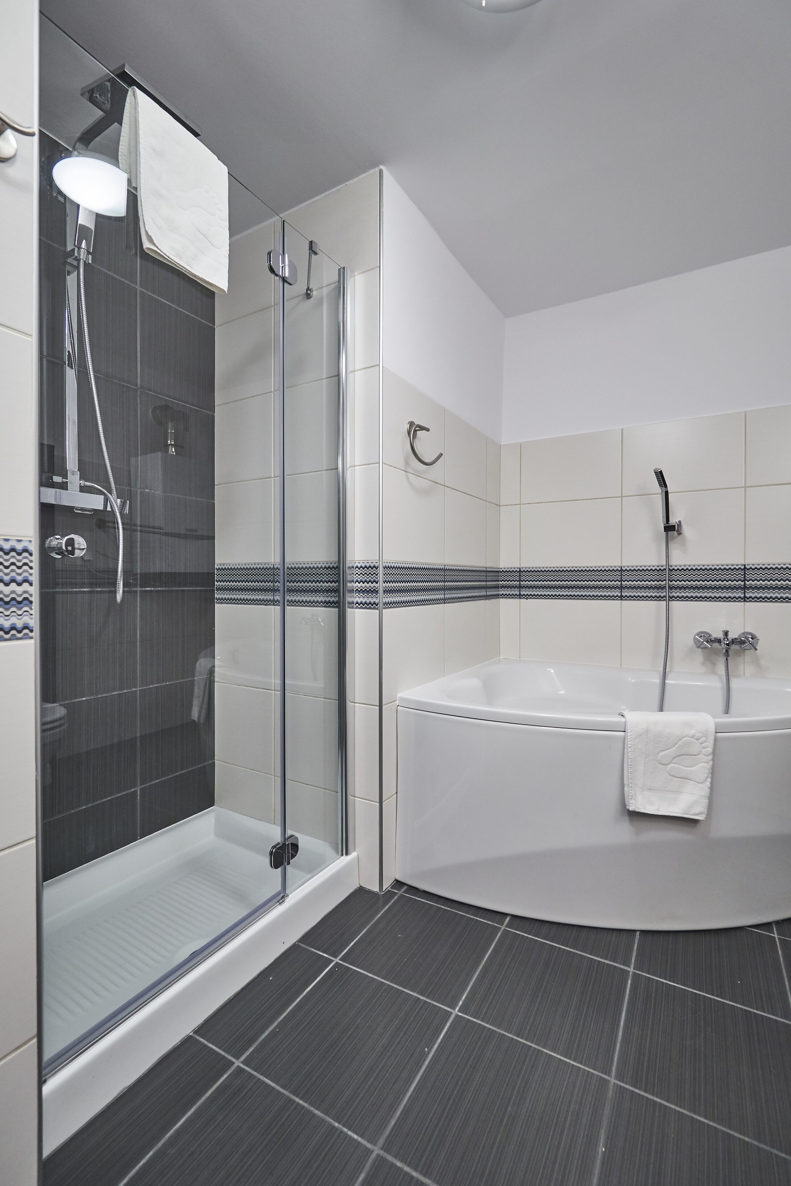 A modern bathroom with a glass-enclosed shower, a freestanding bathtub, and tiled walls.