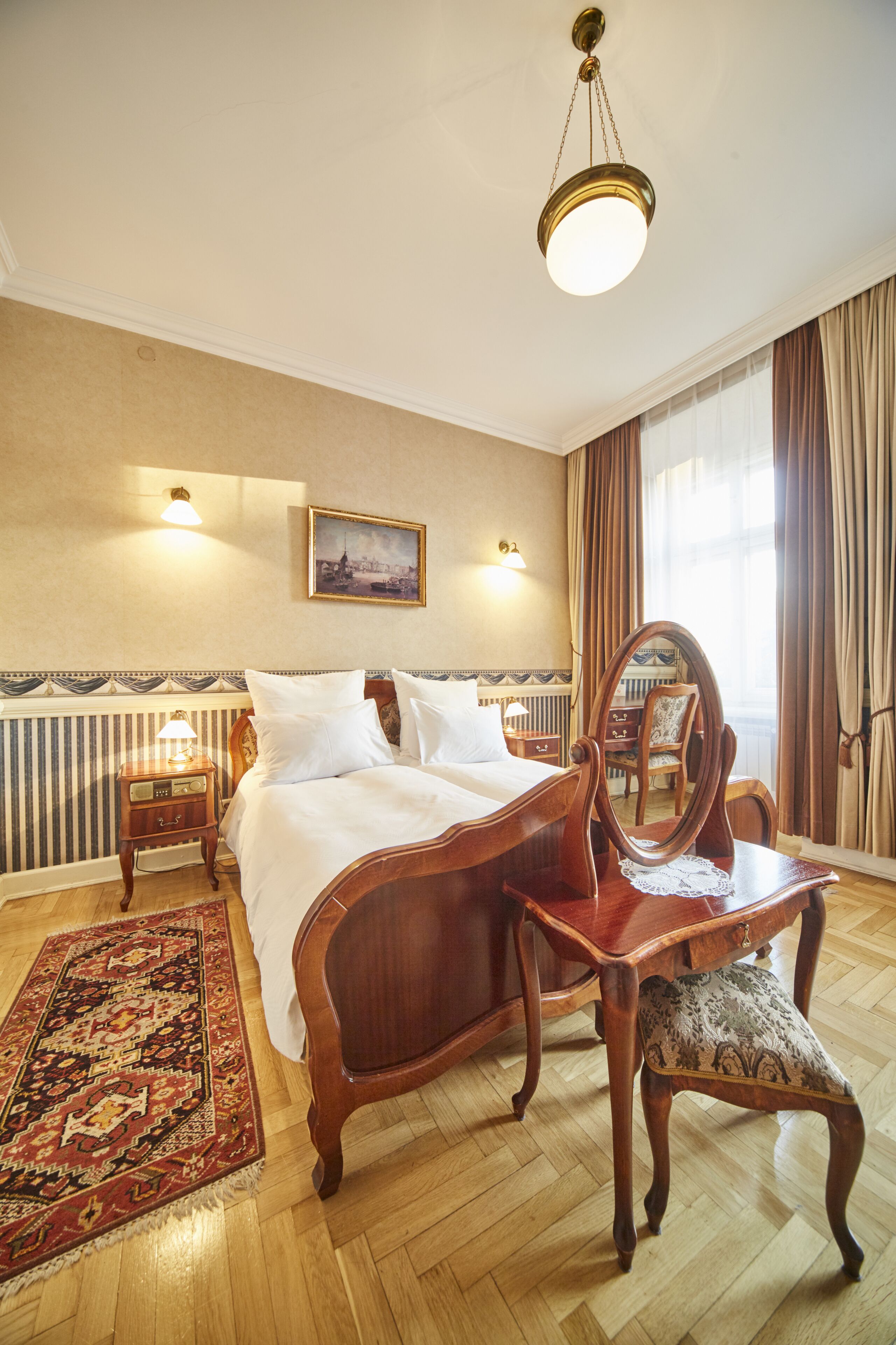 Une chambre d’hôtel avec un grand lit, une commode en bois, un miroir, une table de chevet et un tapis à motifs.