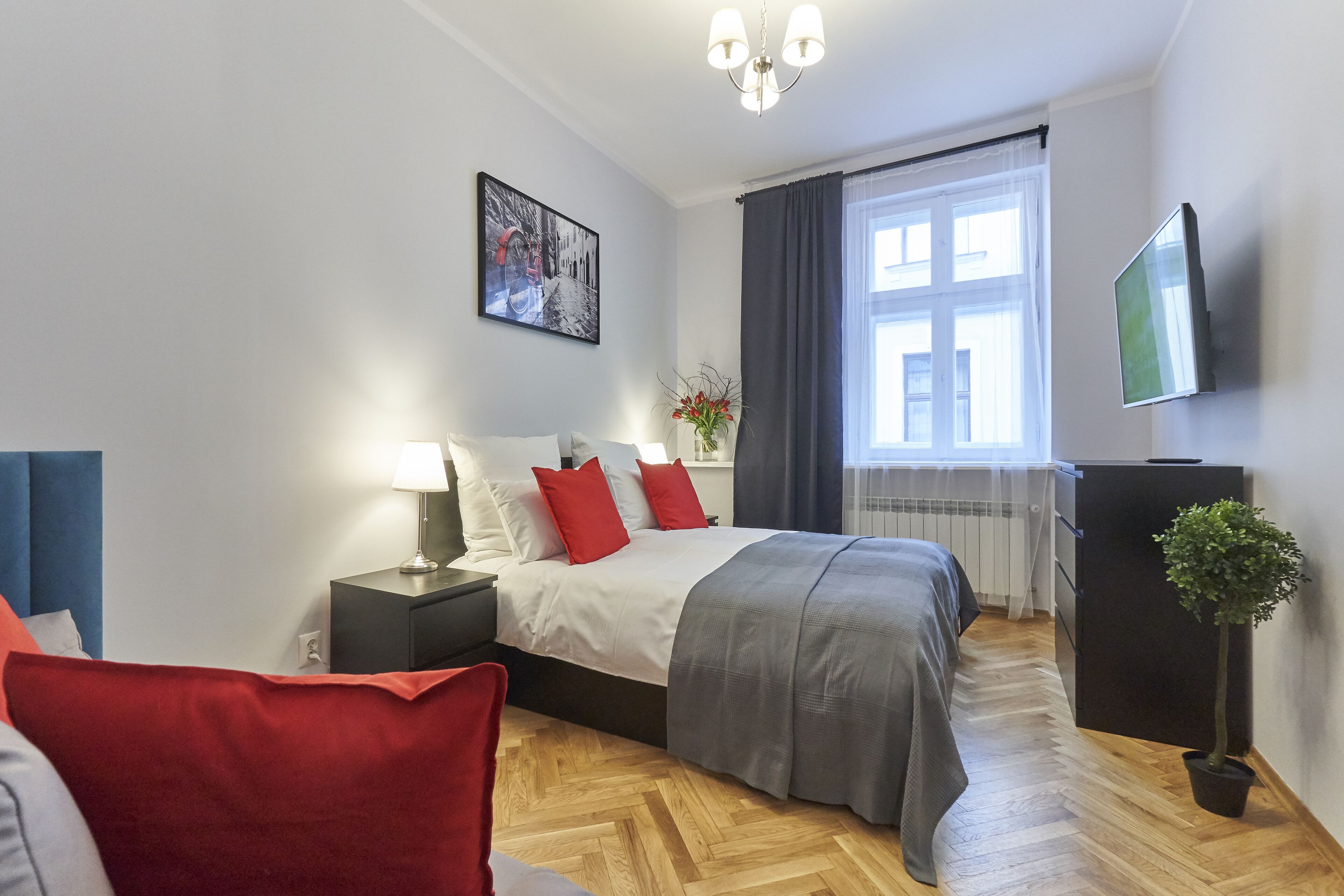Ein modernes Hotelzimmer mit Bett, Nachttischen, Fernseher, Blumentopf und einem Fenster mit Vorhängen.