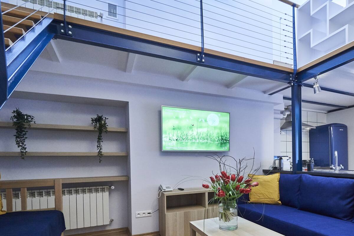 A modern living room with a blue sofa, a wooden coffee table, a flat-screen TV, and a kitchen area in the background.