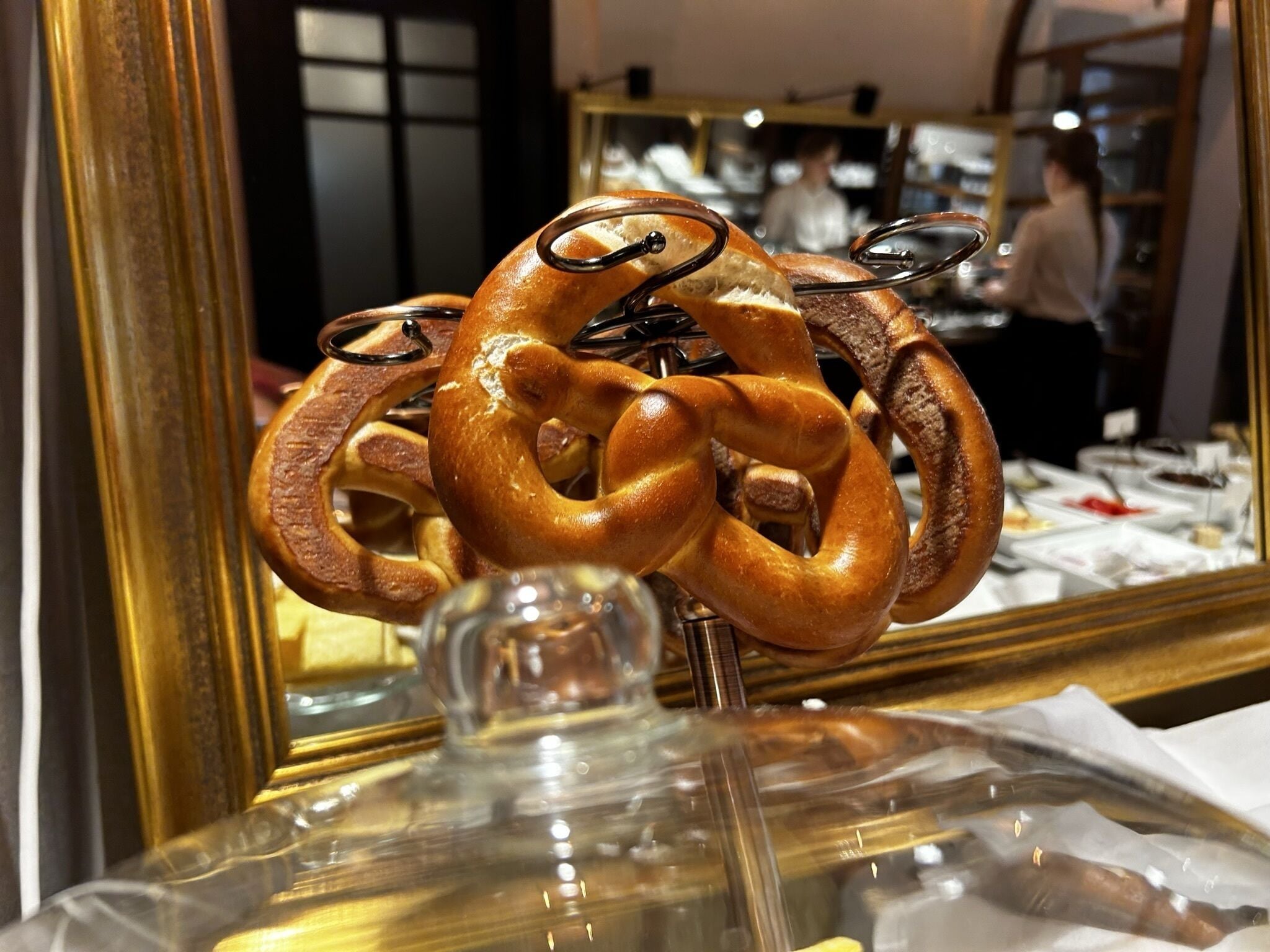 A pretzel with a unique twisted design, displayed on a stand in a bakery setting.