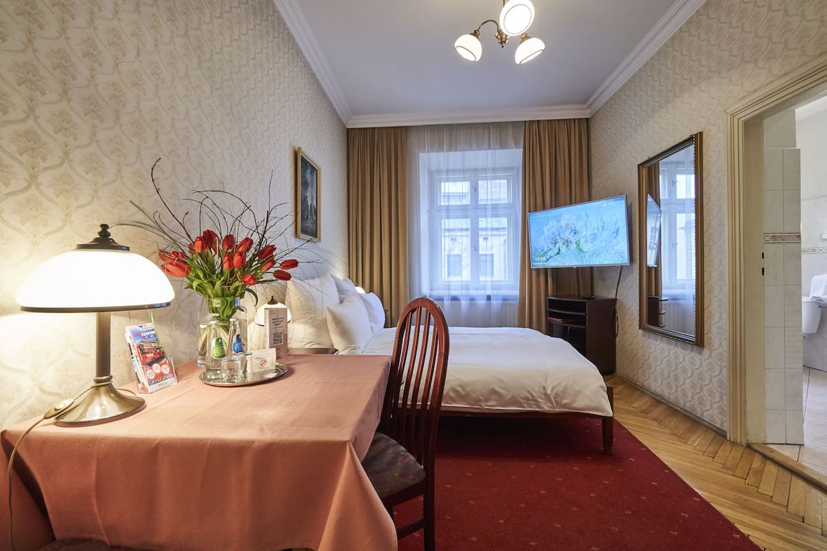 A hotel room with a bed, a desk with a lamp, a TV, and a mirror.