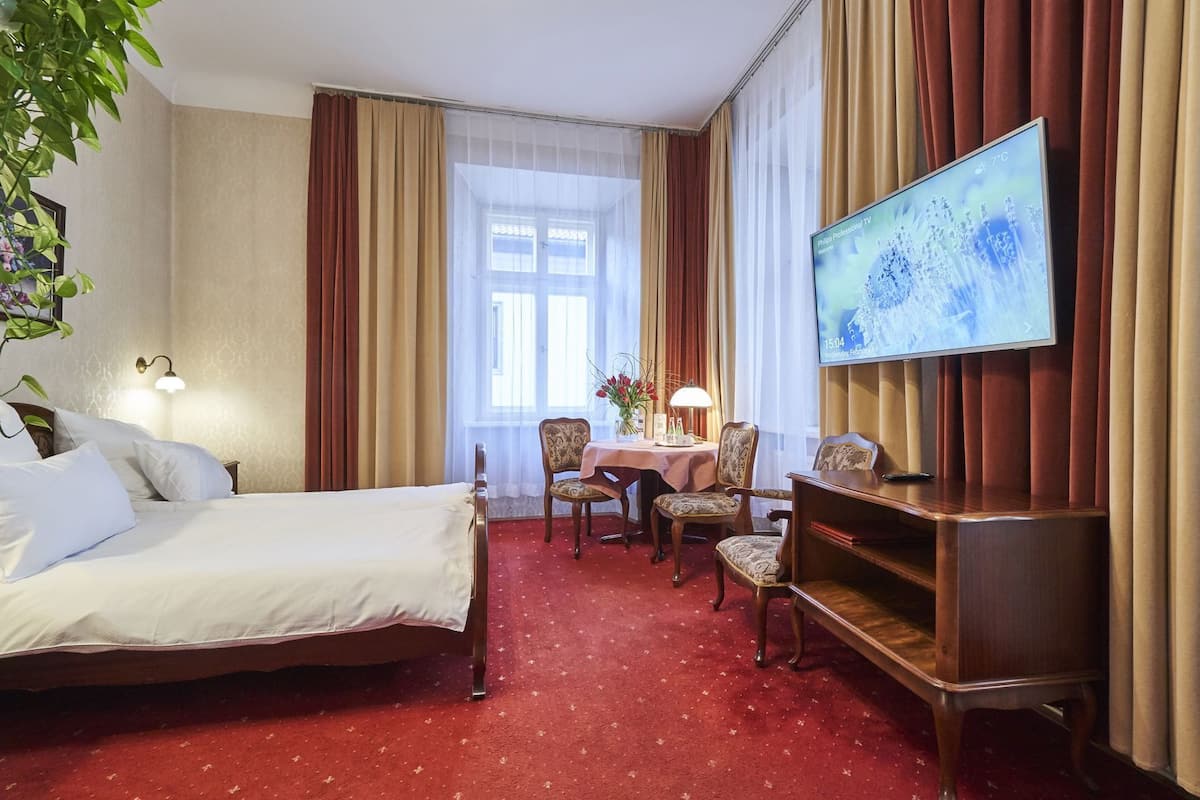 A hotel room with a bed, a desk, a TV, and a window with curtains.