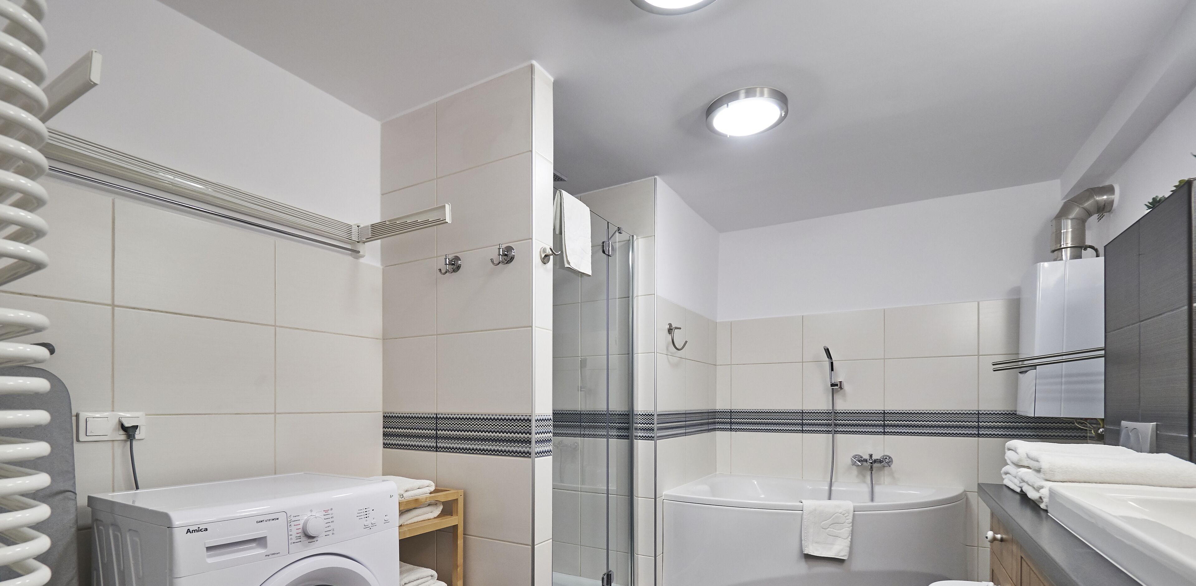 A modern bathroom with a washing machine, a glass shower enclosure, and a bathtub.