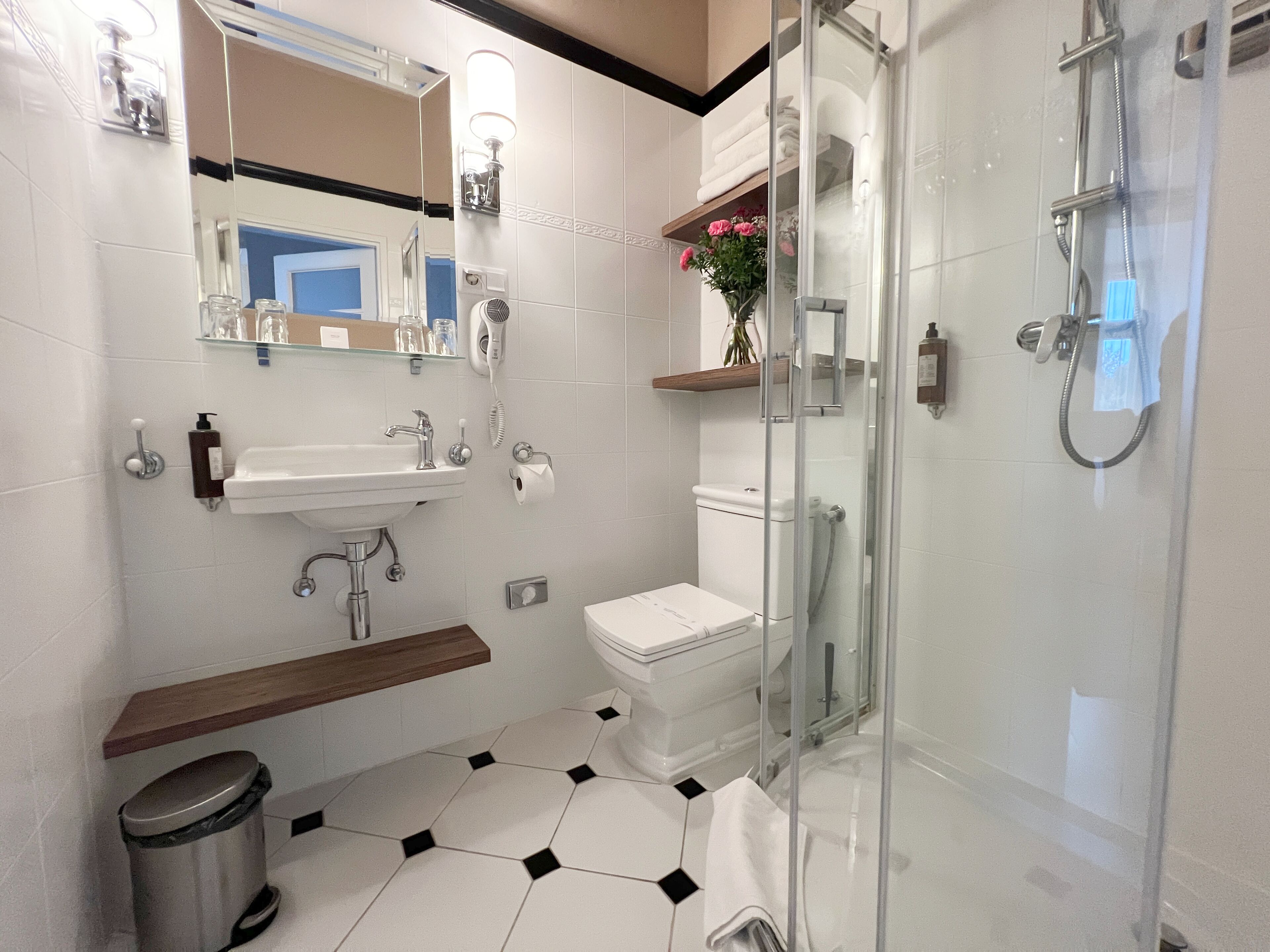 A modern bathroom with a glass-enclosed shower, a white sink with a wooden shelf, and a toilet with a white lid.