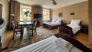 Habitació d'hotel amb un llit, un escriptori amb cadira, una televisió i una finestra gran amb cortines.