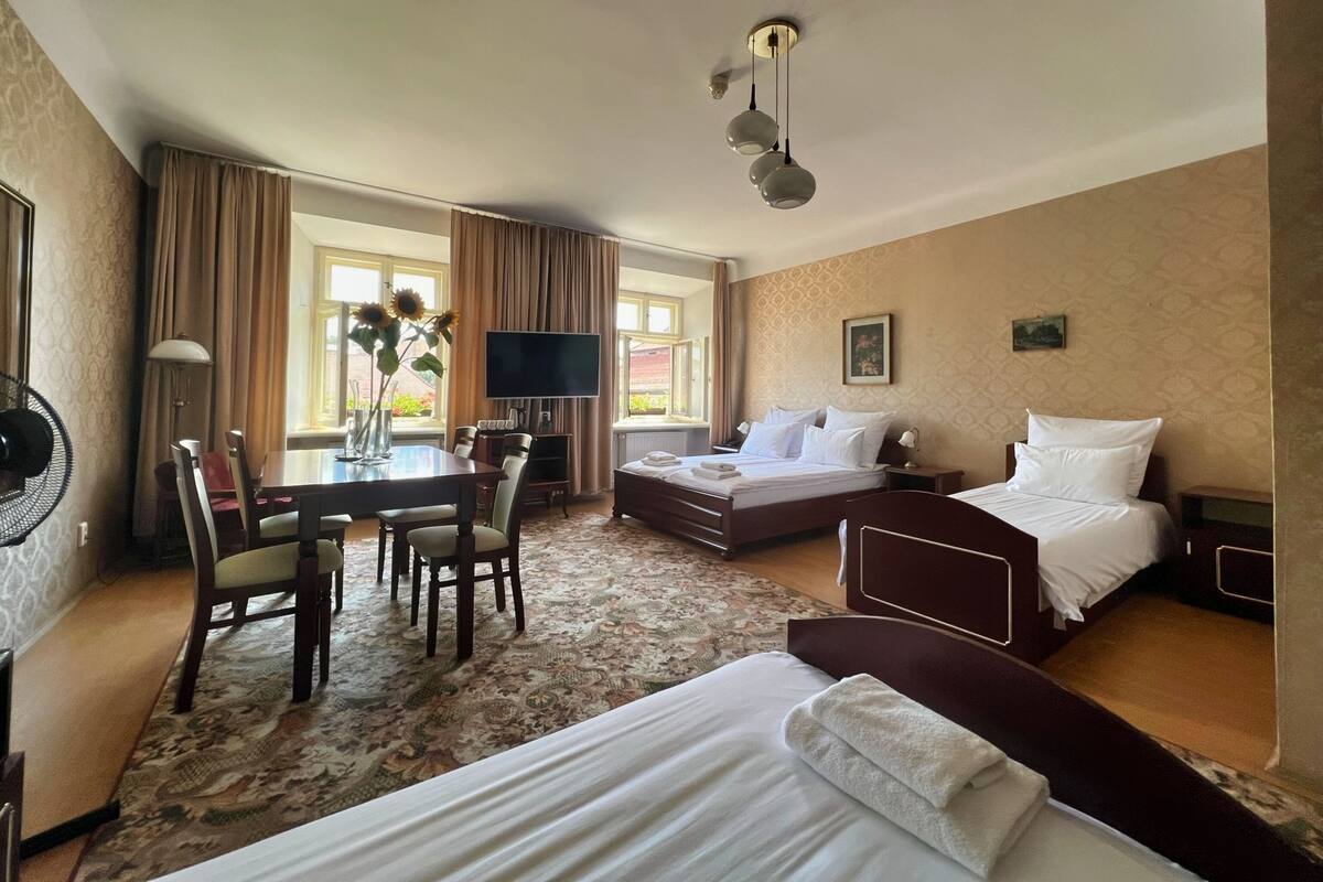 A hotel room with a bed, a desk with a chair, a TV, and a large window with curtains.