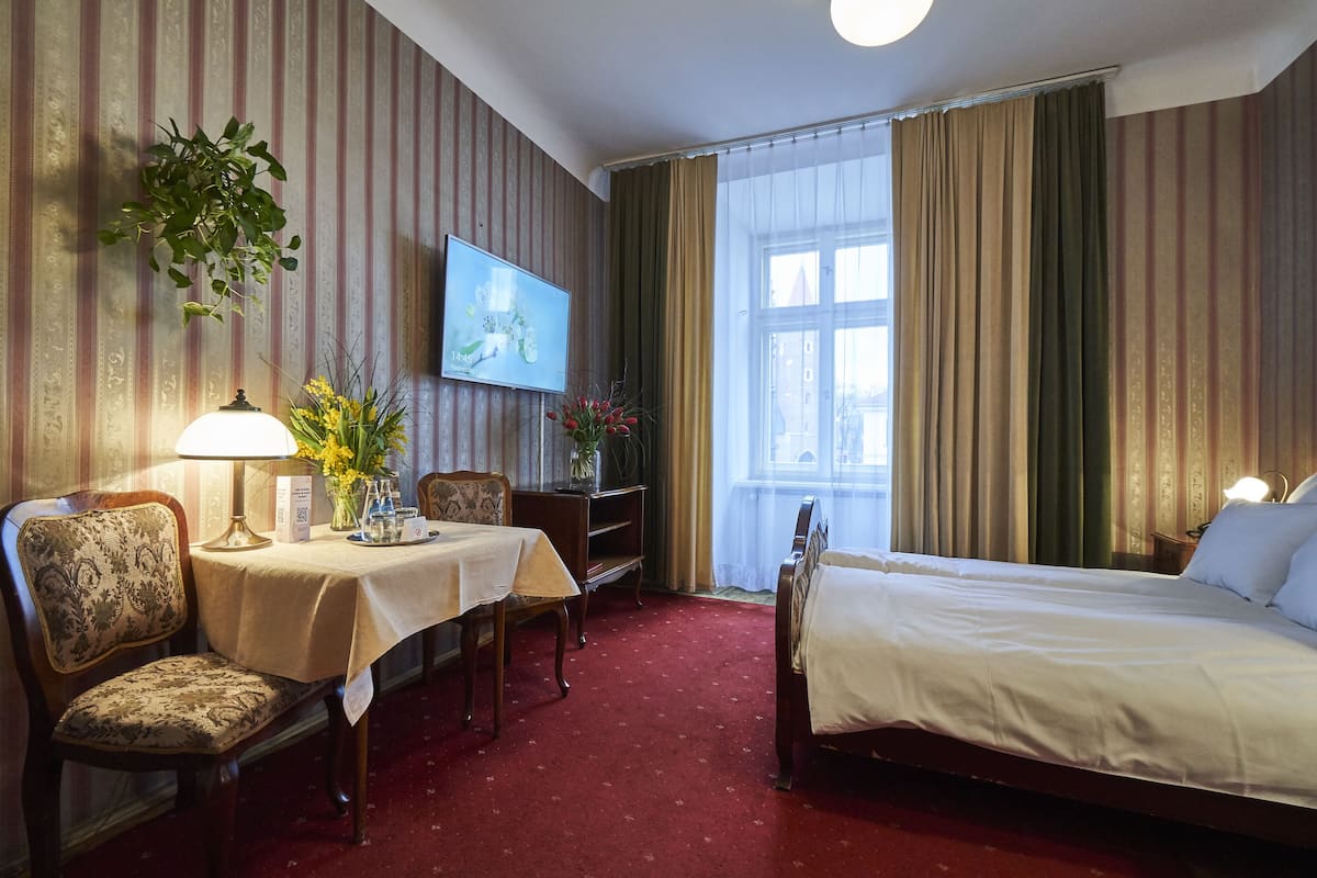 A hotel room with a bed, a desk with a lamp, a chair, a TV, and a window with curtains.