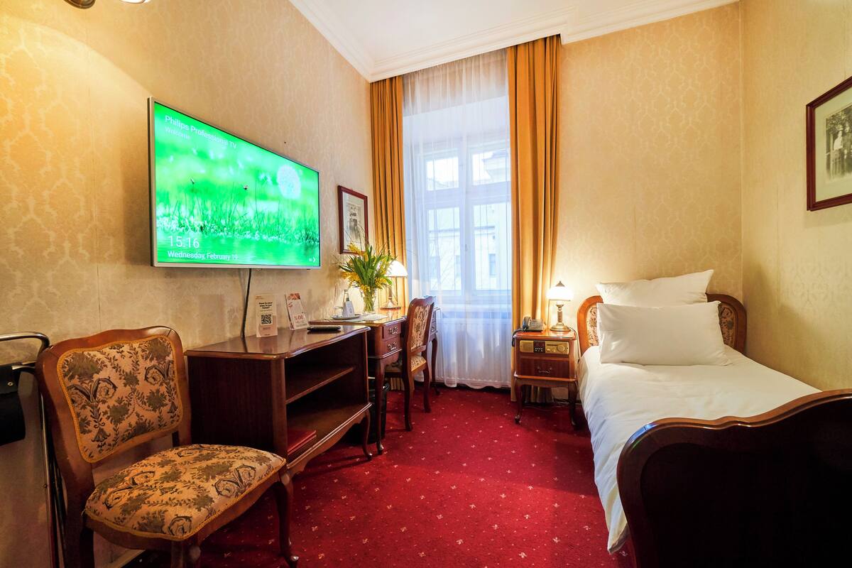 A hotel room with a bed, a desk with a chair, a television, and a window with curtains.
