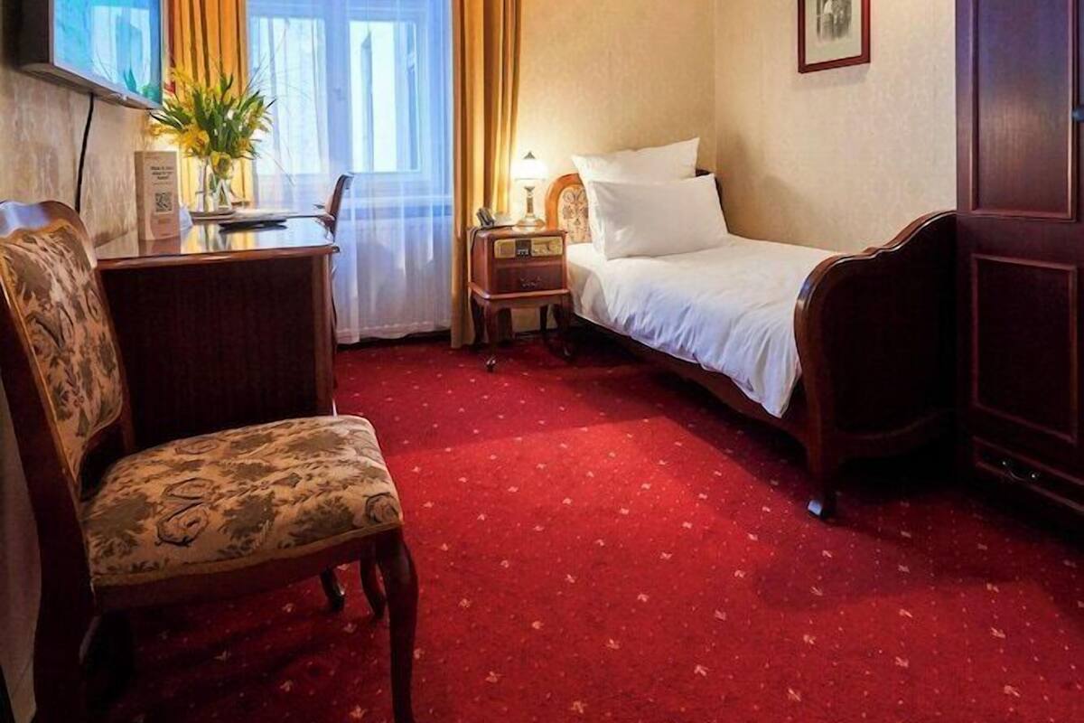 A hotel room with a bed, a desk, a chair, a TV, and a window with curtains.