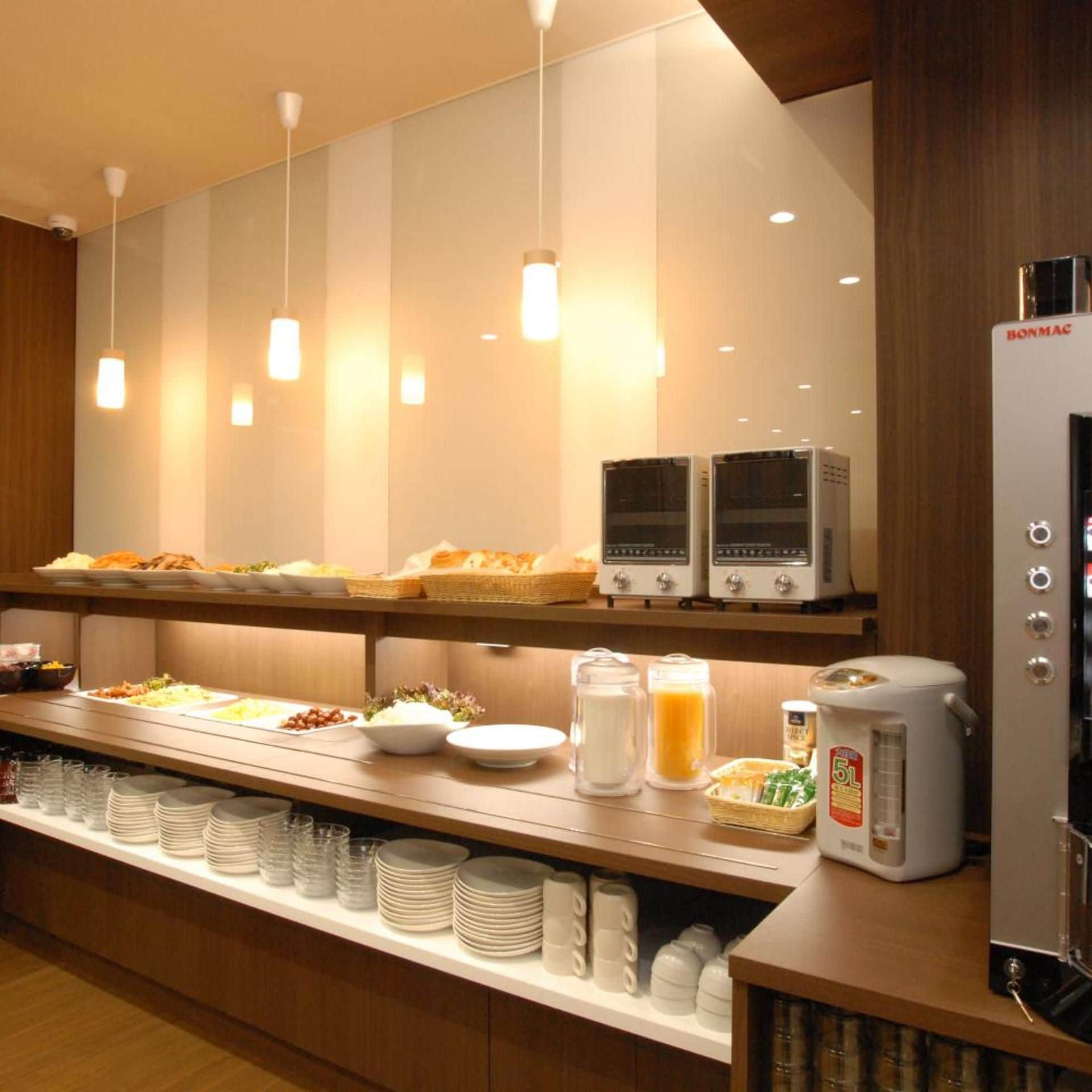 A buffet area with various food items, a coffee machine, and a refrigerator.