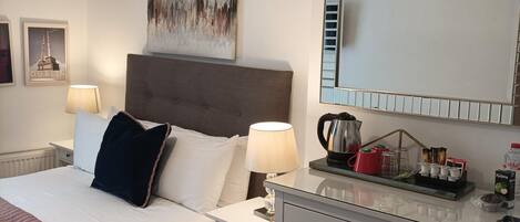 A hotel room with a bed, bedside table, lamp, and a dresser with a mirror.
