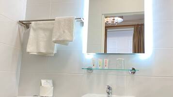 Un baño con inodoro, lavabo y espejo con luz. Hay dos toallas colgadas en un perchero.