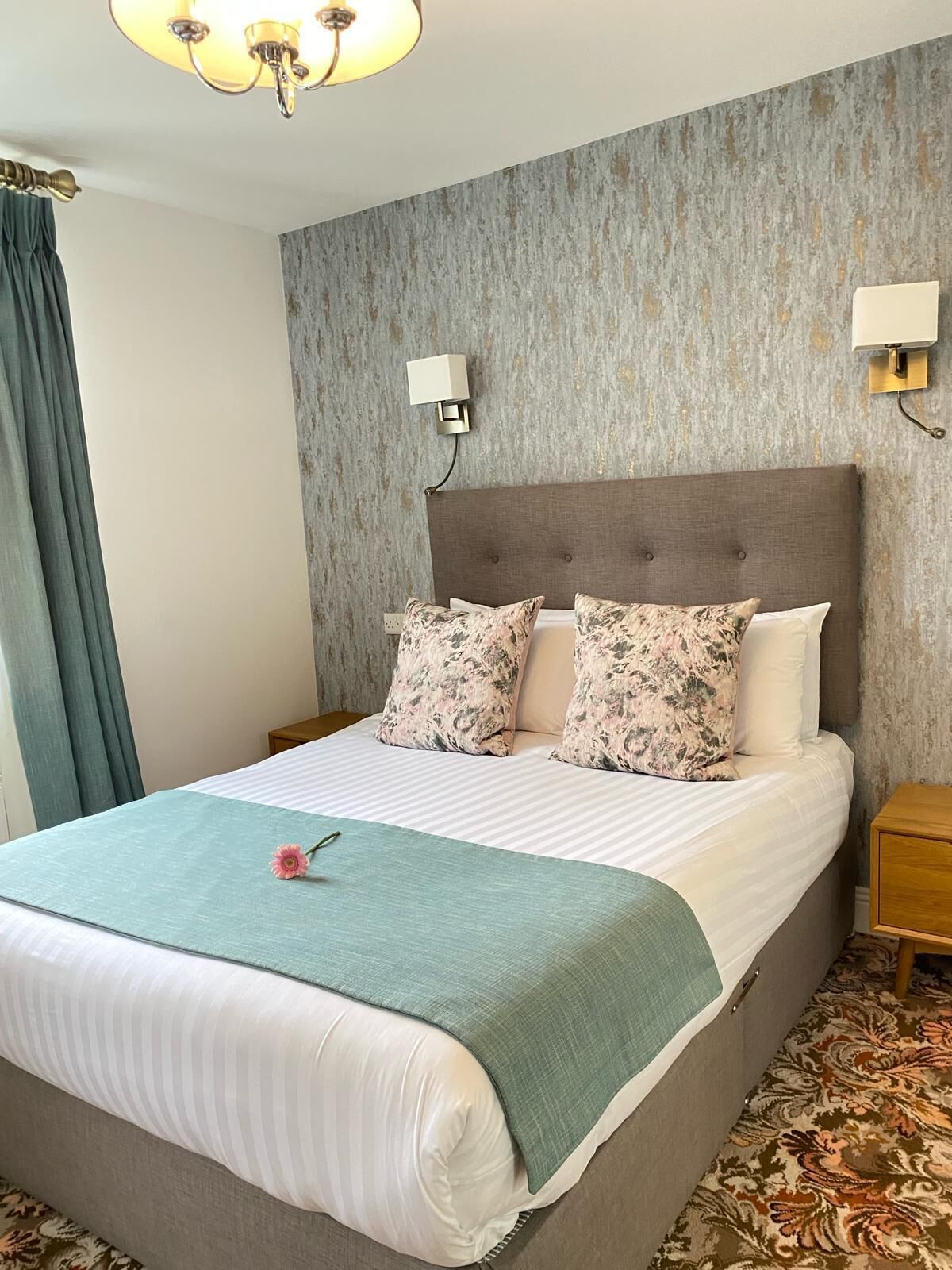 A neatly made bed with floral pillows, a green throw blanket, and a nightstand with a lamp.