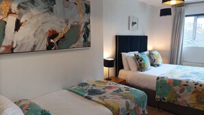 A hotel room with two beds, a large abstract painting, a framed picture, and a window with curtains. - Tom Dick and Harriet's (Dublin)