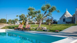 Una piscina con sillas de descanso, un edificio de piedra y una zona verde con árboles.