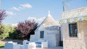 Un edificio de piedra con techo cónico y un balcón. Hay muebles de exterior blancos frente al edificio.