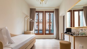 A modern hotel room with a bed, a desk, a chair, a mirror, and a view of the building outside. - Numa Venice Palazzo Orseolo (Venice)