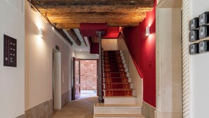 A hallway with a red wall, a wooden ceiling, and a staircase with red steps. There are signs indicating room numbers and a door to the right. - Numa Venice Palazzo Orseolo (Venice)