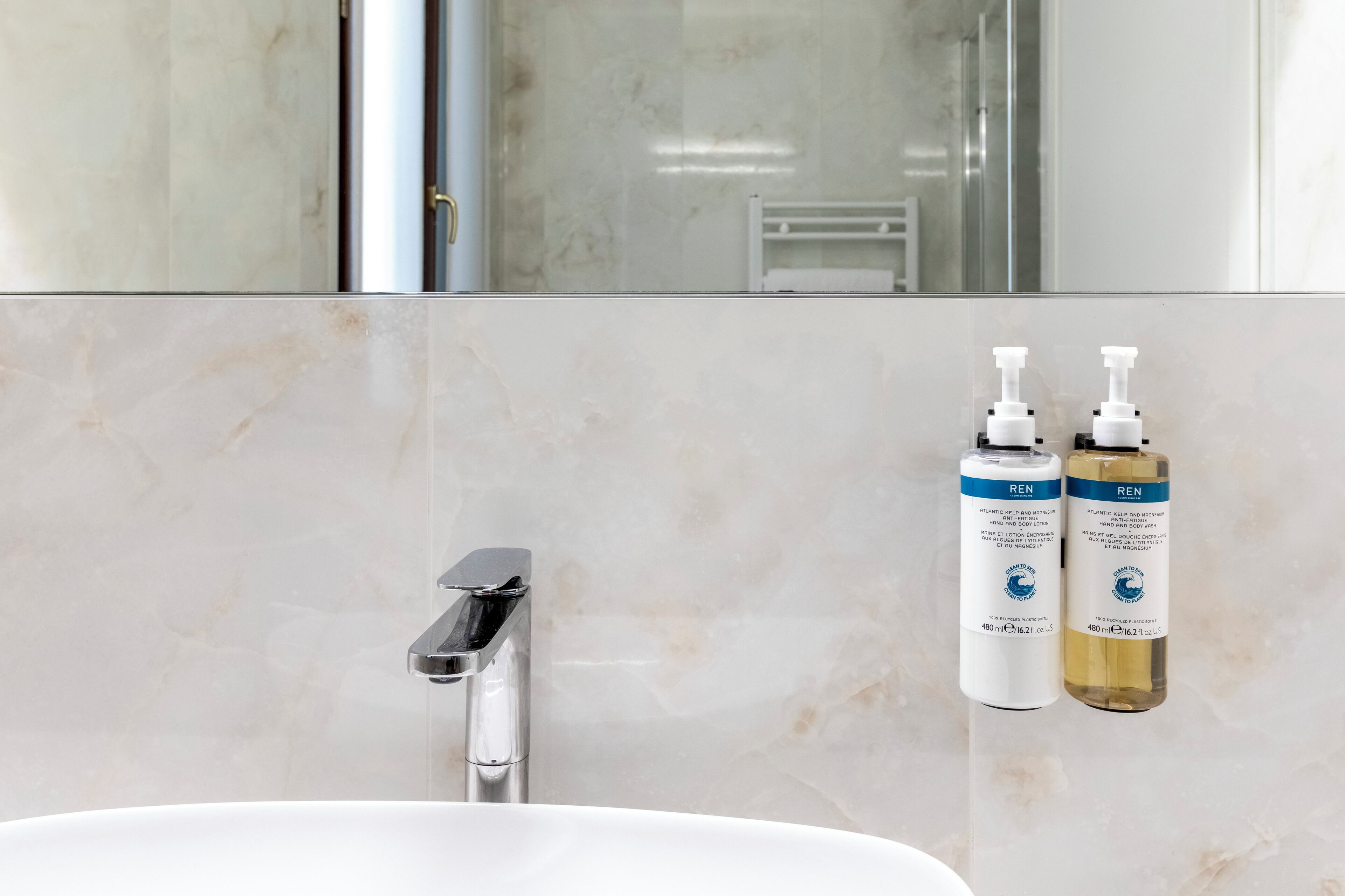 A bathroom with a marble sink, a modern faucet, and two bottles of REN hand and body lotion.