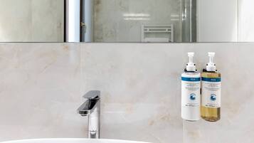 A bathroom with a marble sink, a modern faucet, and two bottles of REN hand and body lotion.