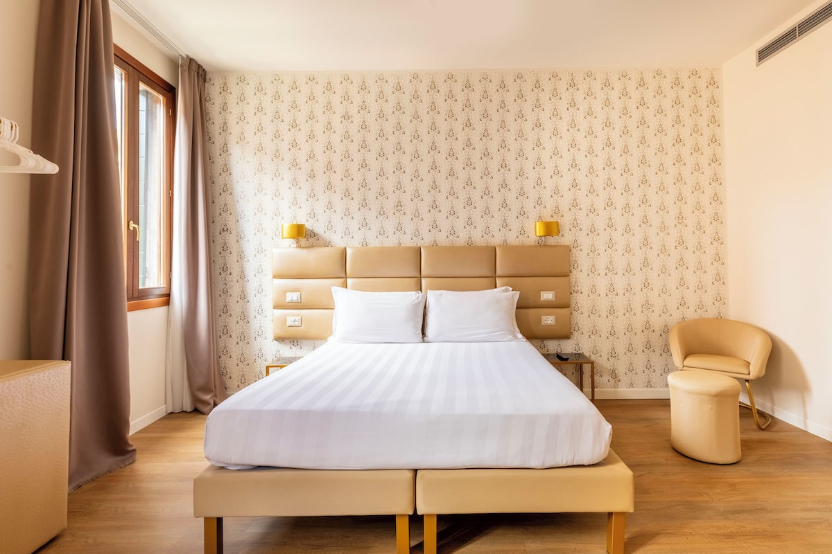 A hotel room with a large bed, bedside tables, a chair, and a window with curtains.